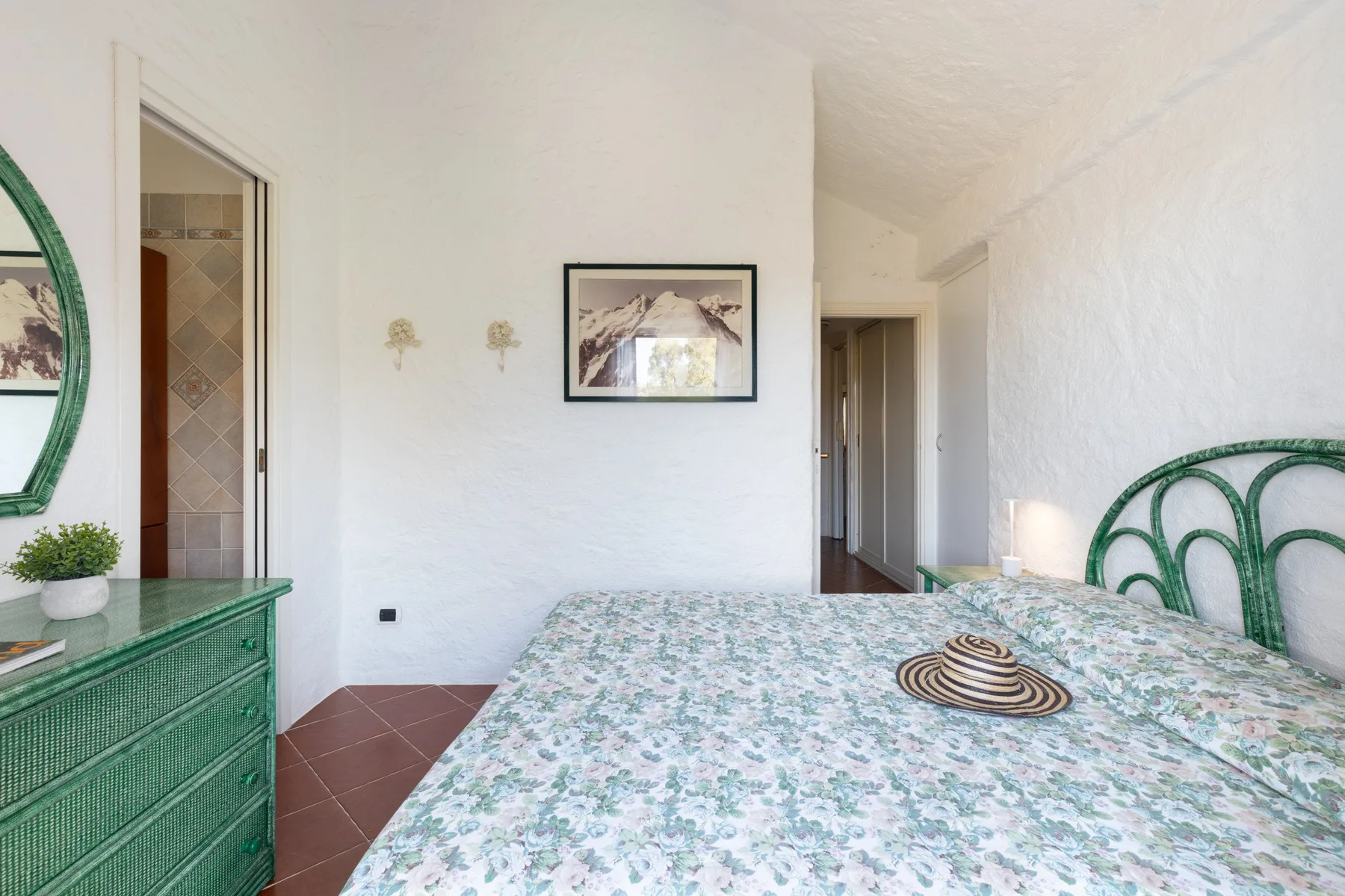 A bedroom with a floral bedspread, green headboard, and matching dresser.