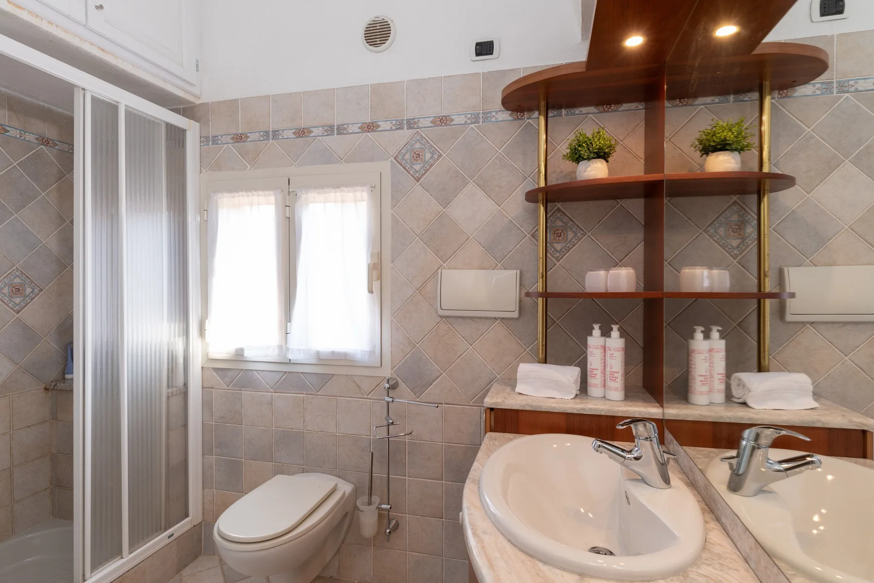 A tiled bathroom with a sink, toilet, and glass shower enclosure.