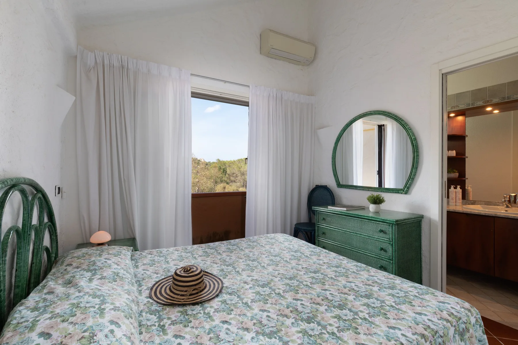 A bedroom with a floral bedspread, green dresser, and open curtains.