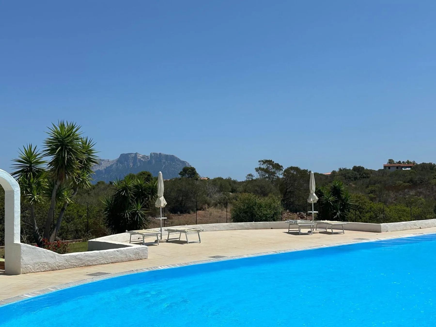 Outdoor swimming pool beside a sunny terrace with loungers and umbrellas.