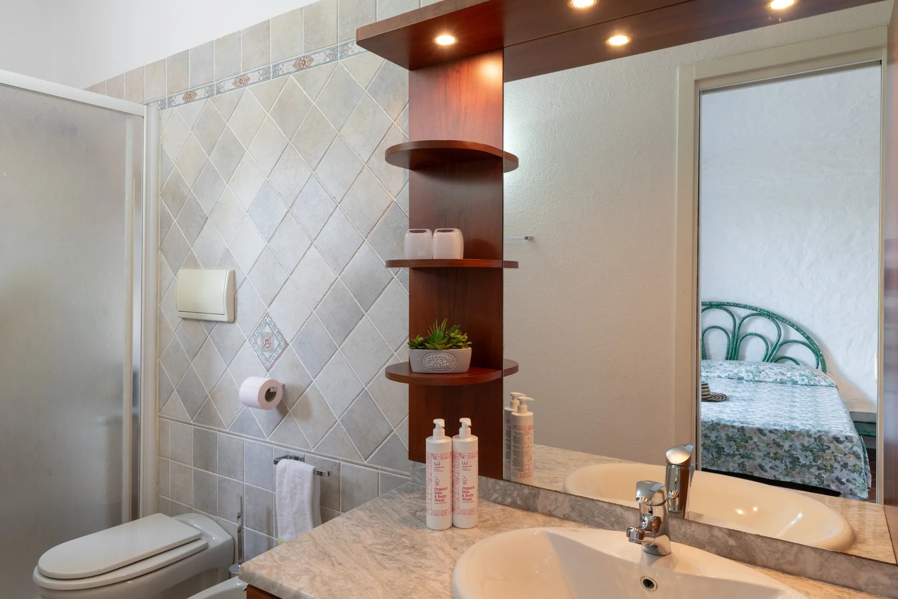 A tiled bathroom vanity with a sink and mirror beside the shower.