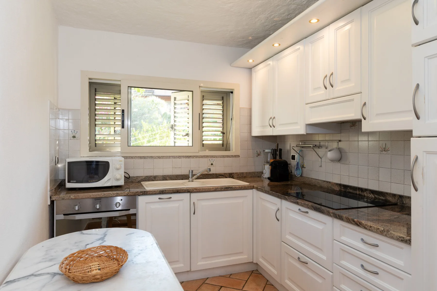 A bright kitchen with white cabinets, a tiled backsplash, and a window above the sink.