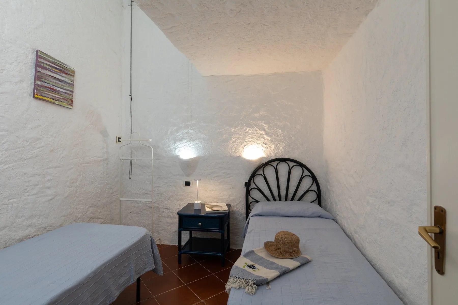 A small bedroom with two single beds, a bedside table, and white textured walls.
