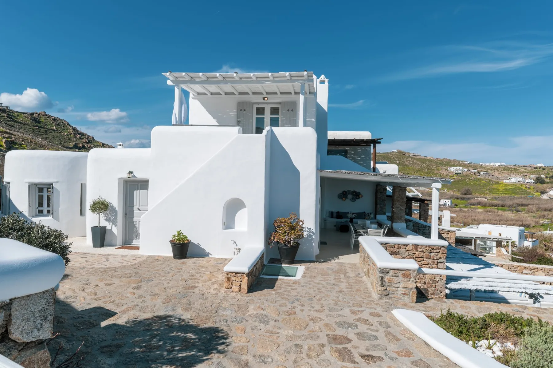 A white villa with a rooftop pergola and a stone-paved courtyard.