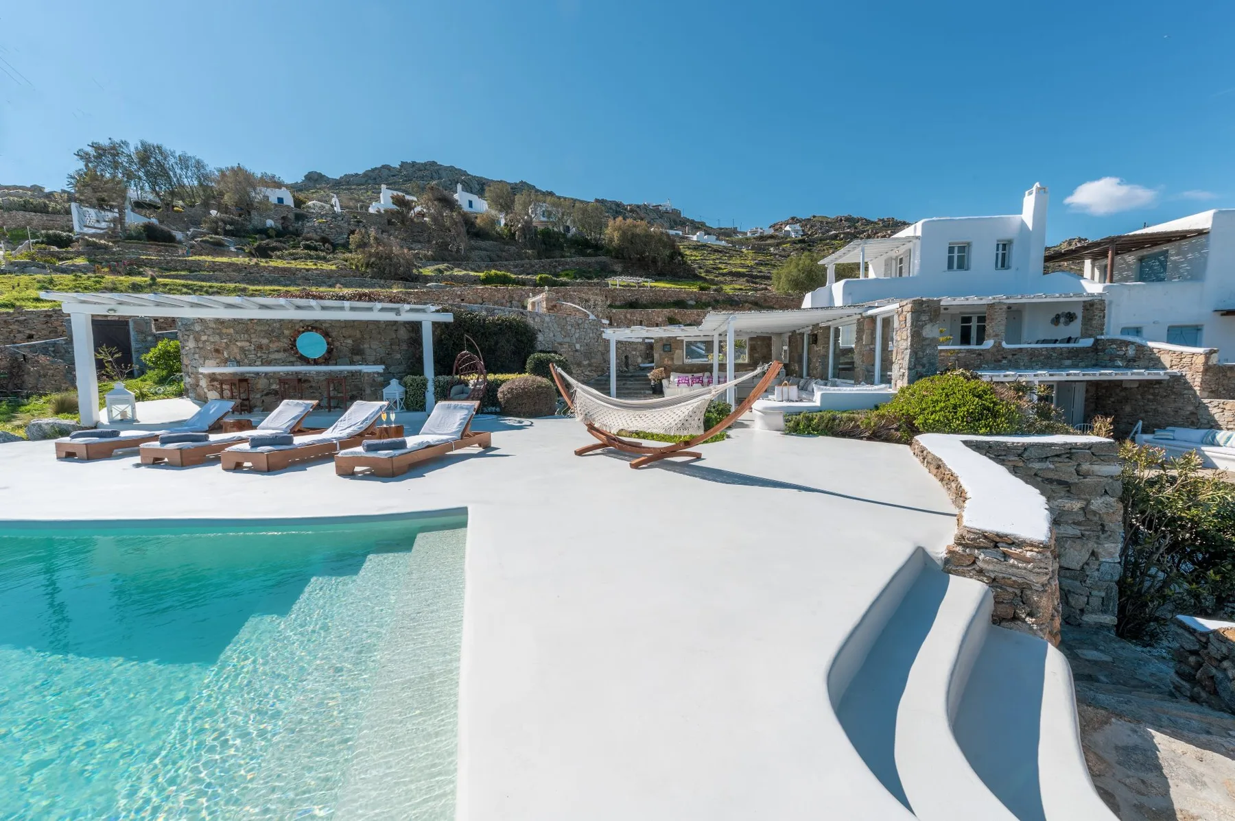 An outdoor pool area with lounge seating and a hammock beside white buildings.