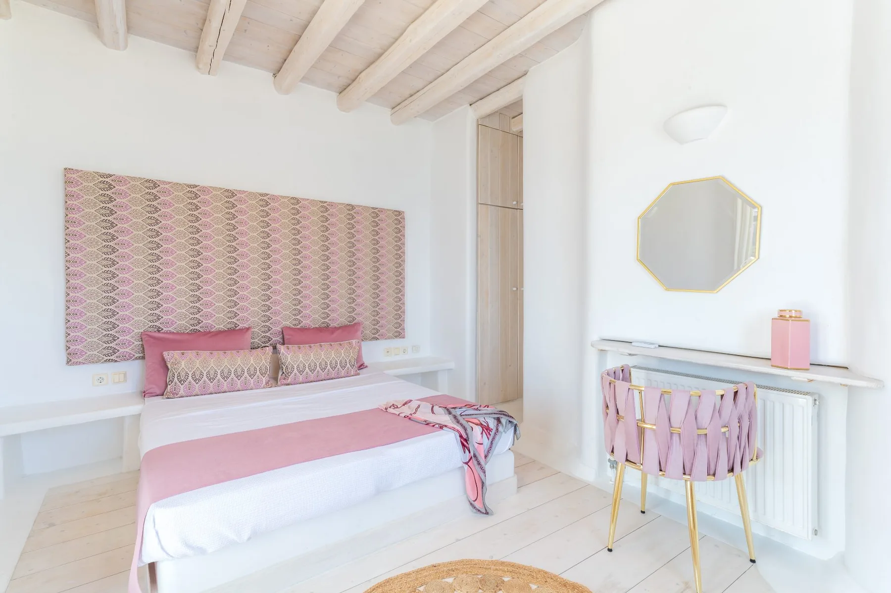 A bright bedroom with a bed and a small desk beneath a mirror.