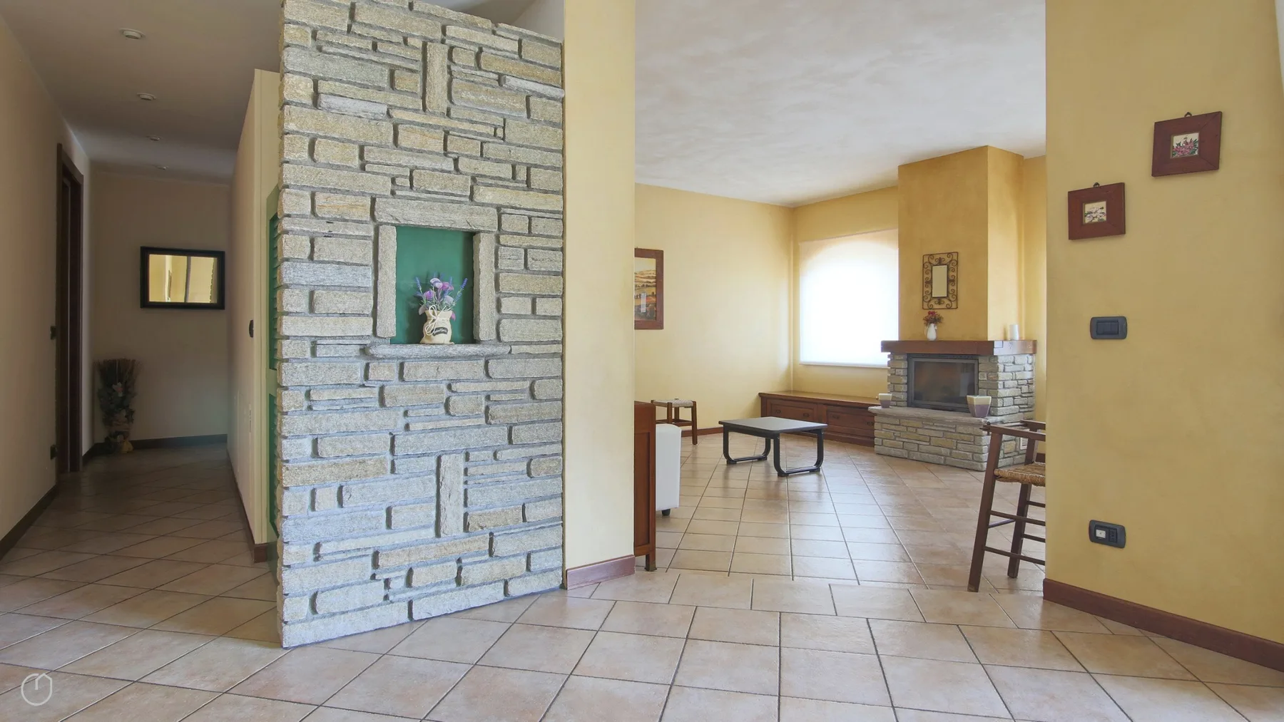 A tiled living room with a stone fireplace and a small seating area.