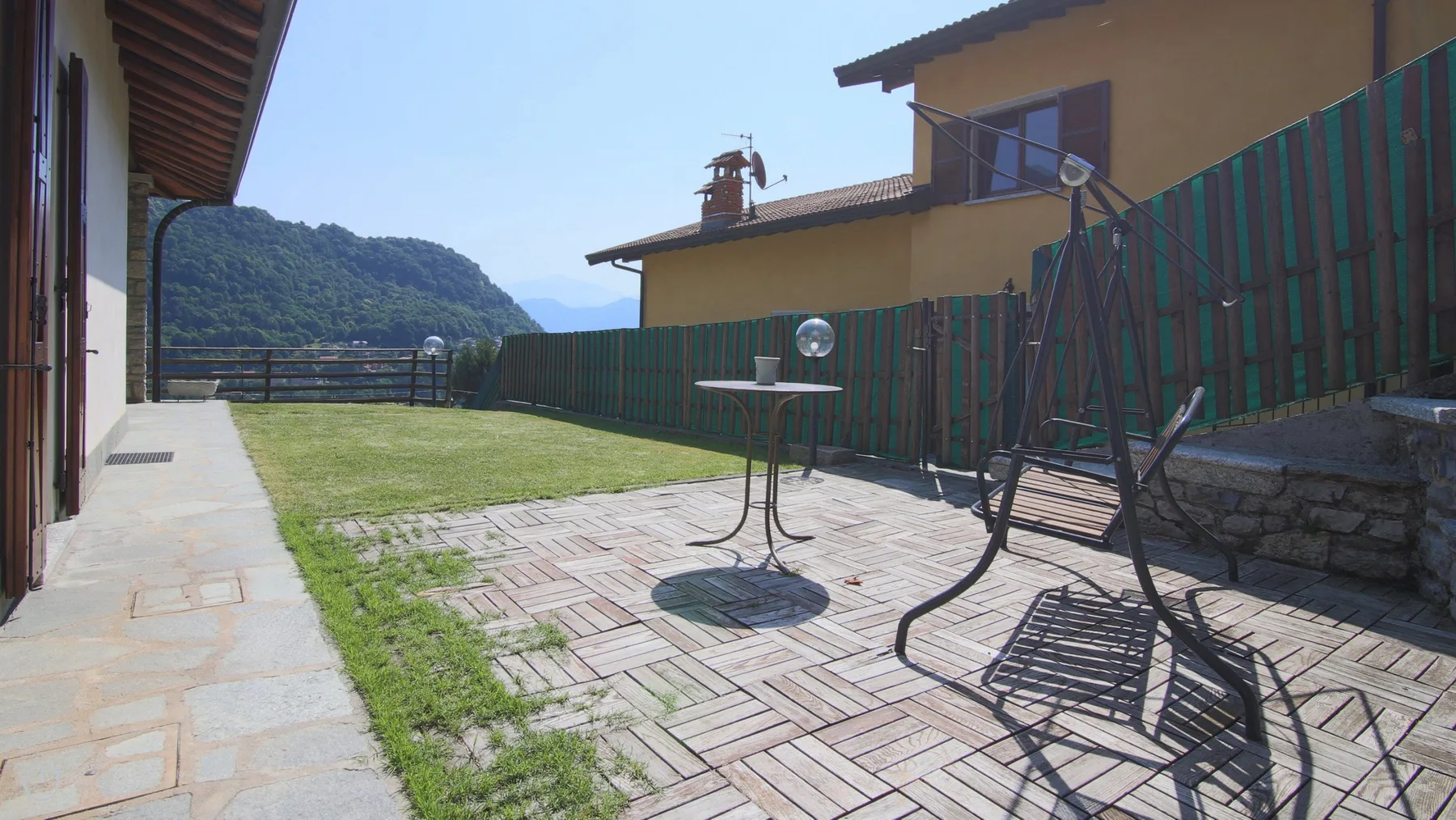 A paved outdoor patio has a small table and a hanging swing.