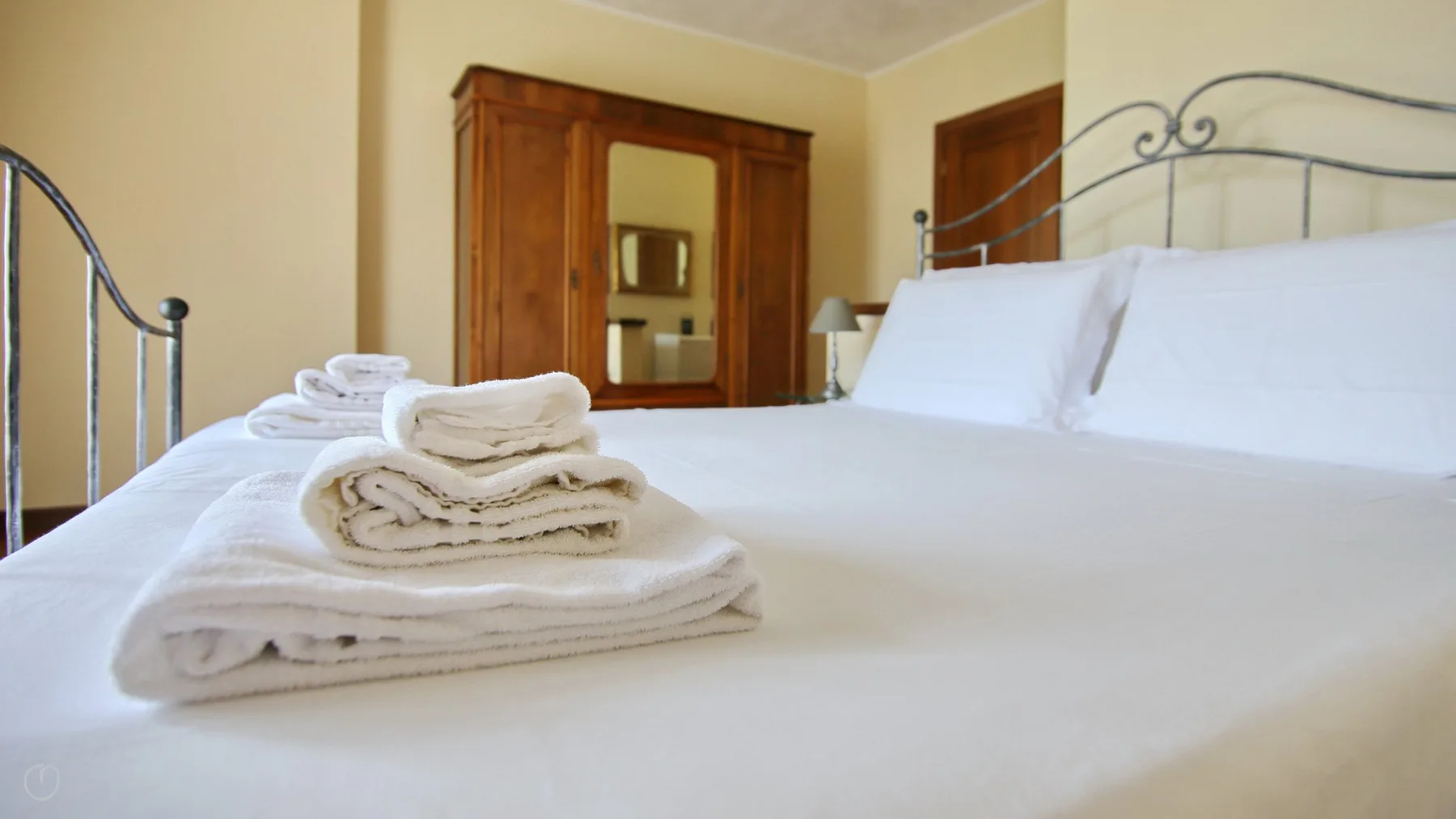 A bedroom with white bedding and folded towels on the bed.
