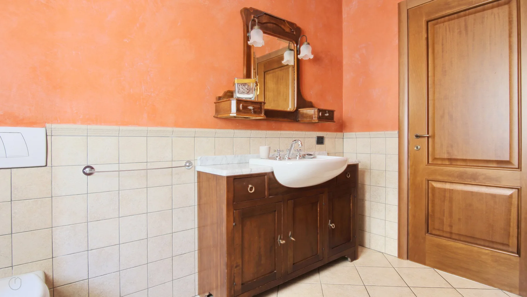 A bathroom with a wooden vanity, white sink, and mirror against orange walls.