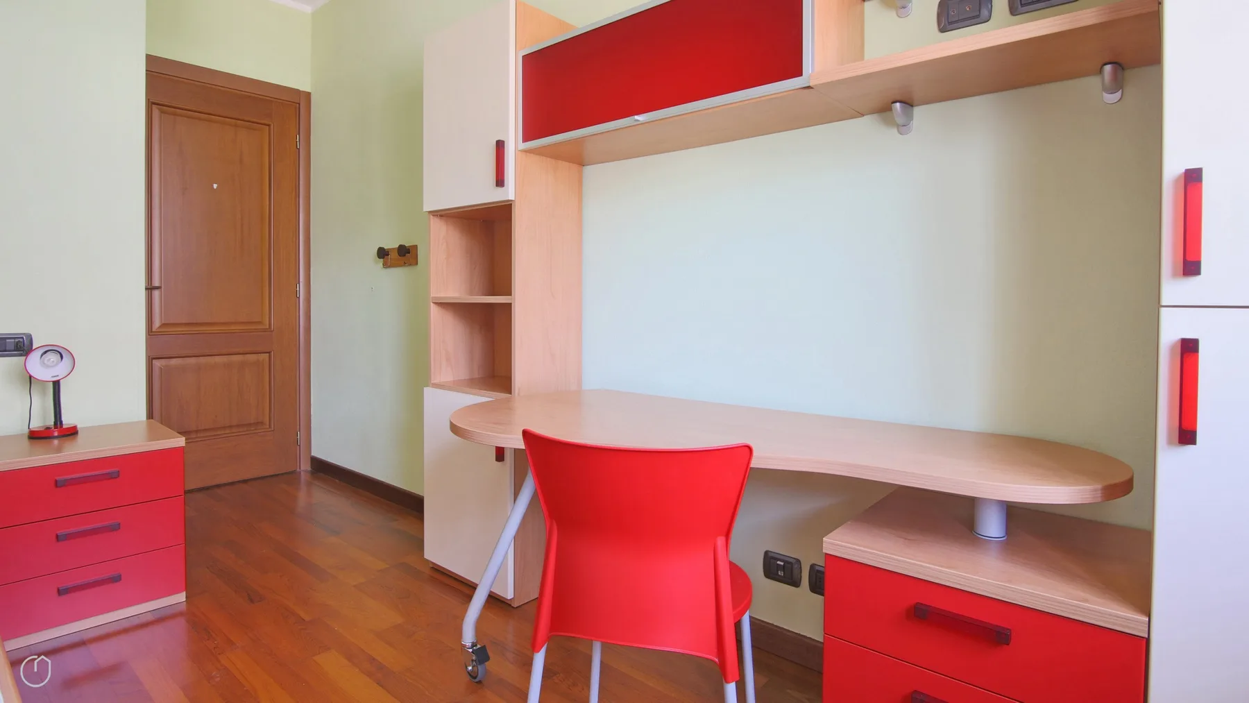 A compact study area features a desk, red chair, and built-in shelving.