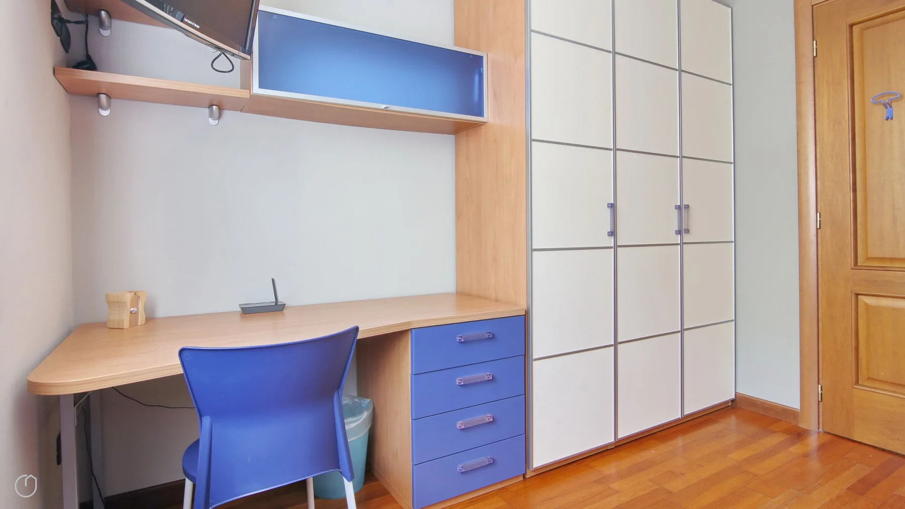 A bedroom workspace with a desk, blue chair, and built-in wardrobes.