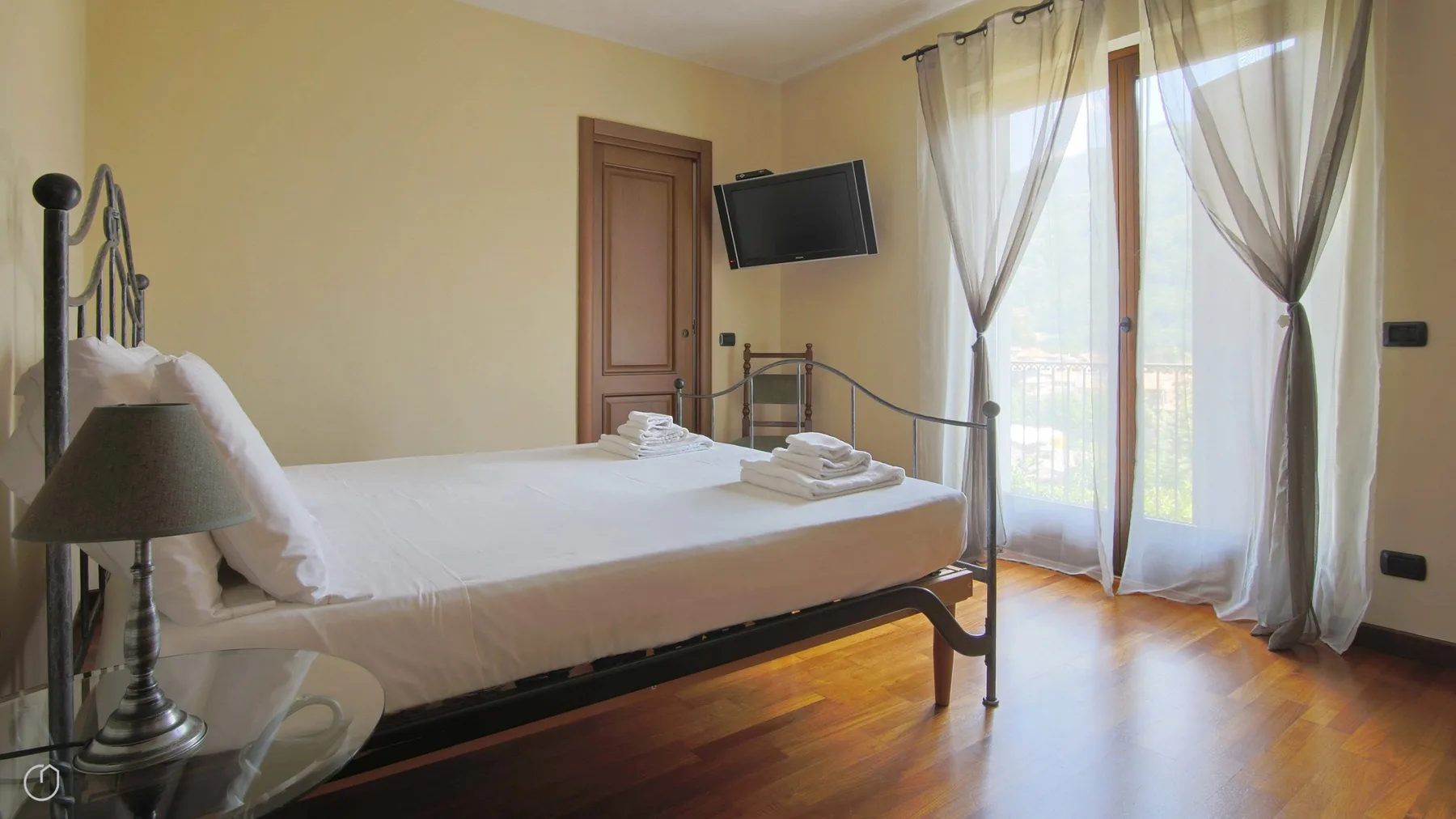 A bedroom with a bed beside tall windows covered by sheer curtains.