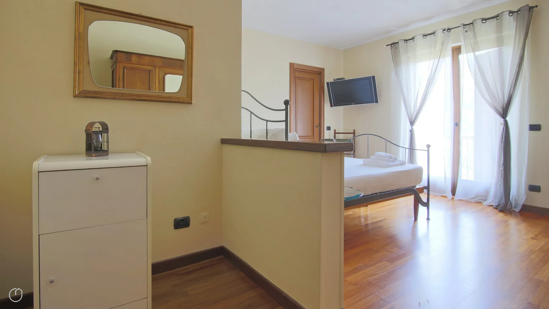 A bedroom with a raised sleeping area, a television, and sheer curtains.