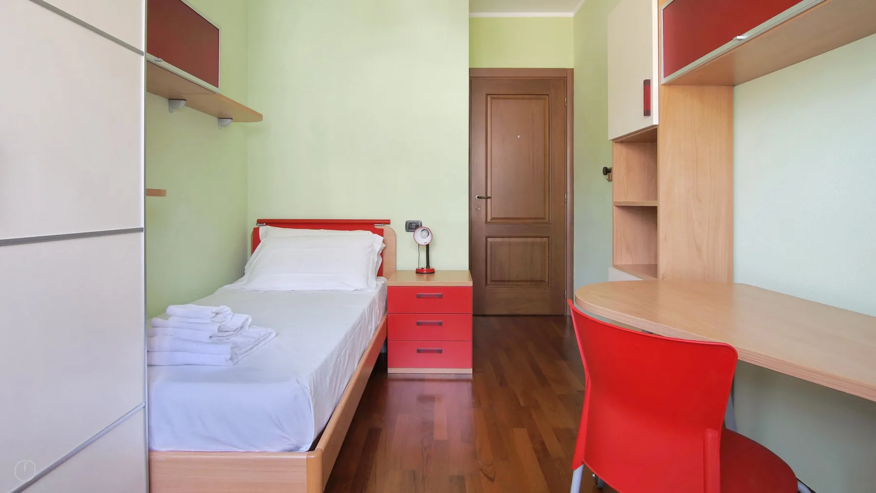 A bedroom with a single bed, red desk chair, and built-in desk.