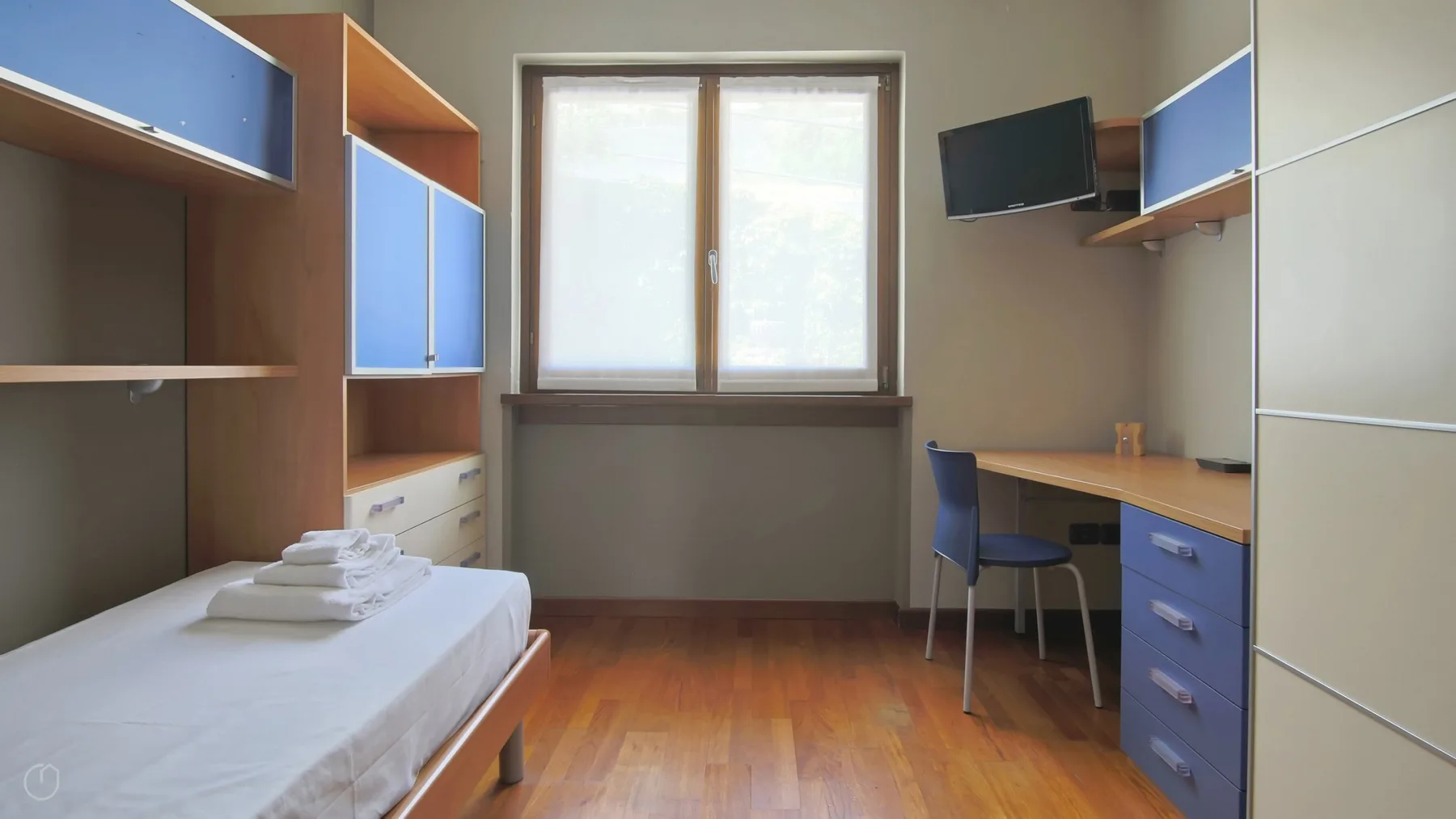 A bedroom with a single bed, built-in storage, and a desk beside the window.