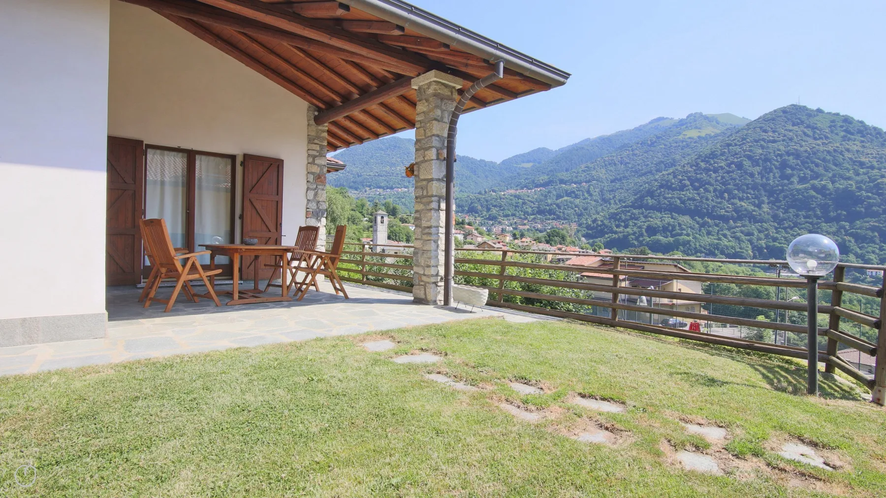 A covered outdoor seating area overlooks a grassy yard and green mountains.