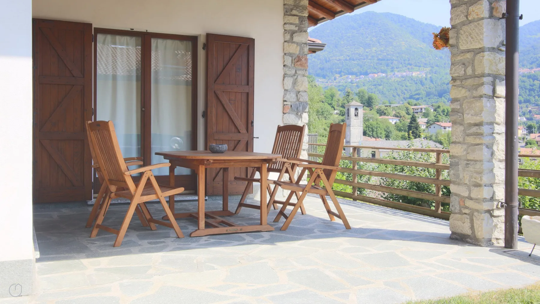 Una terraza de piedra con asientos de madera da a un valle verde.