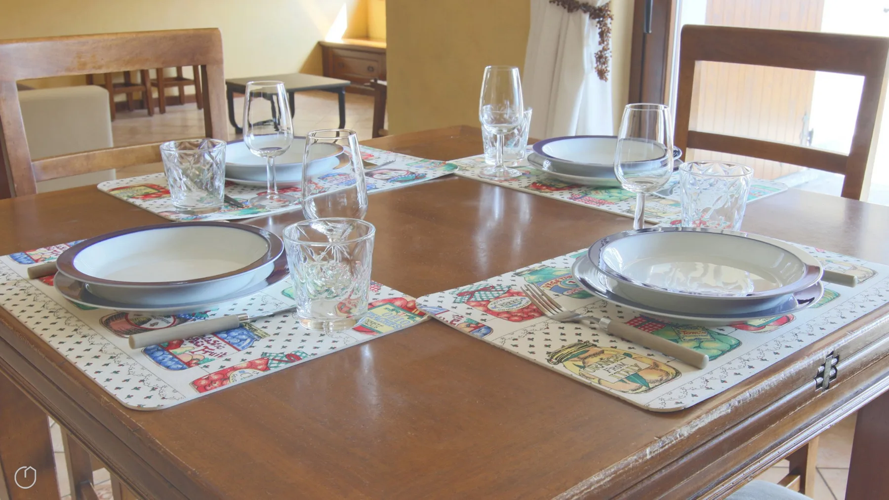 A wooden dining table is set with plates, glasses, and colorful placemats.