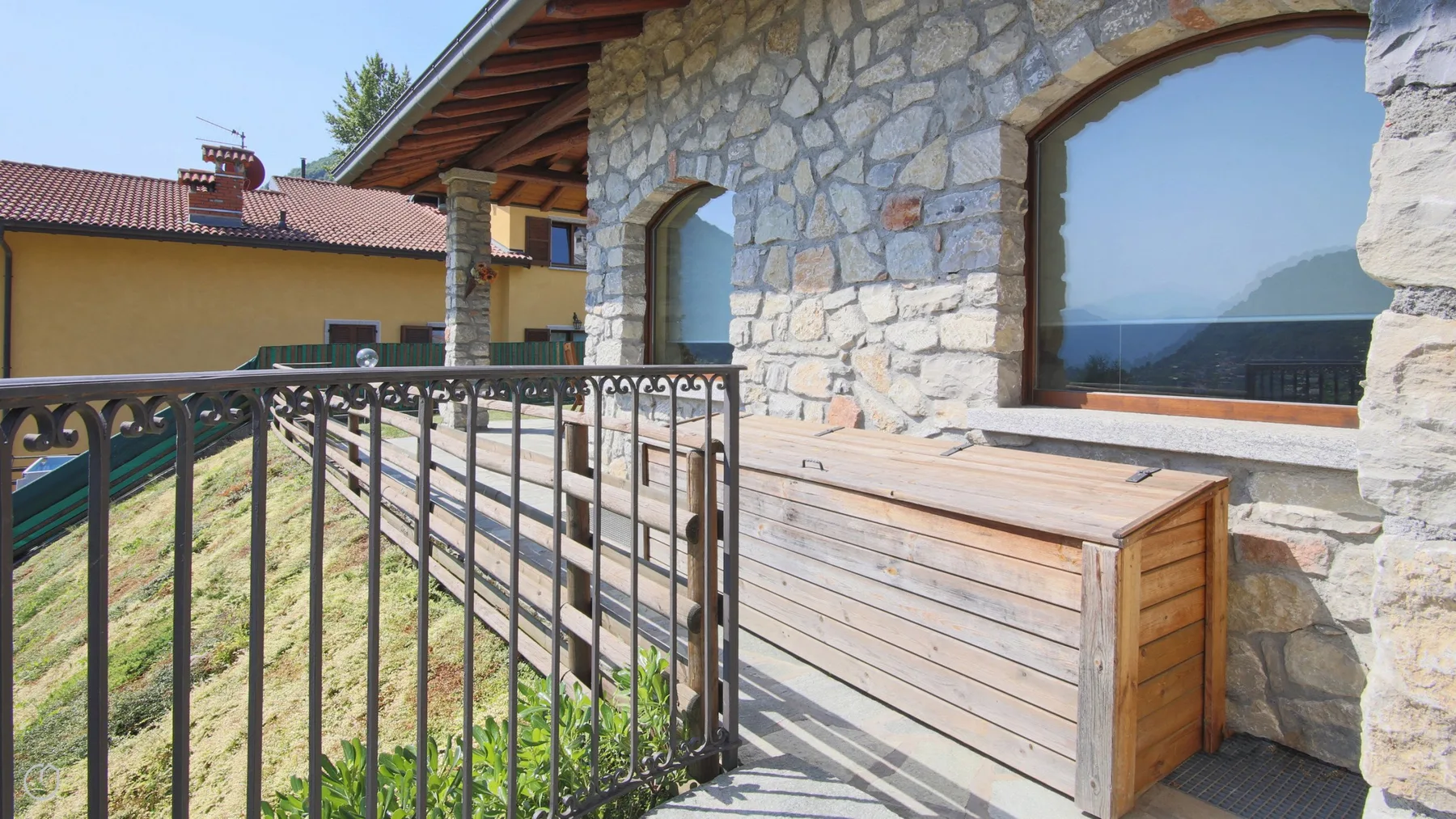 A stone exterior patio with a wooden storage box and metal railing.