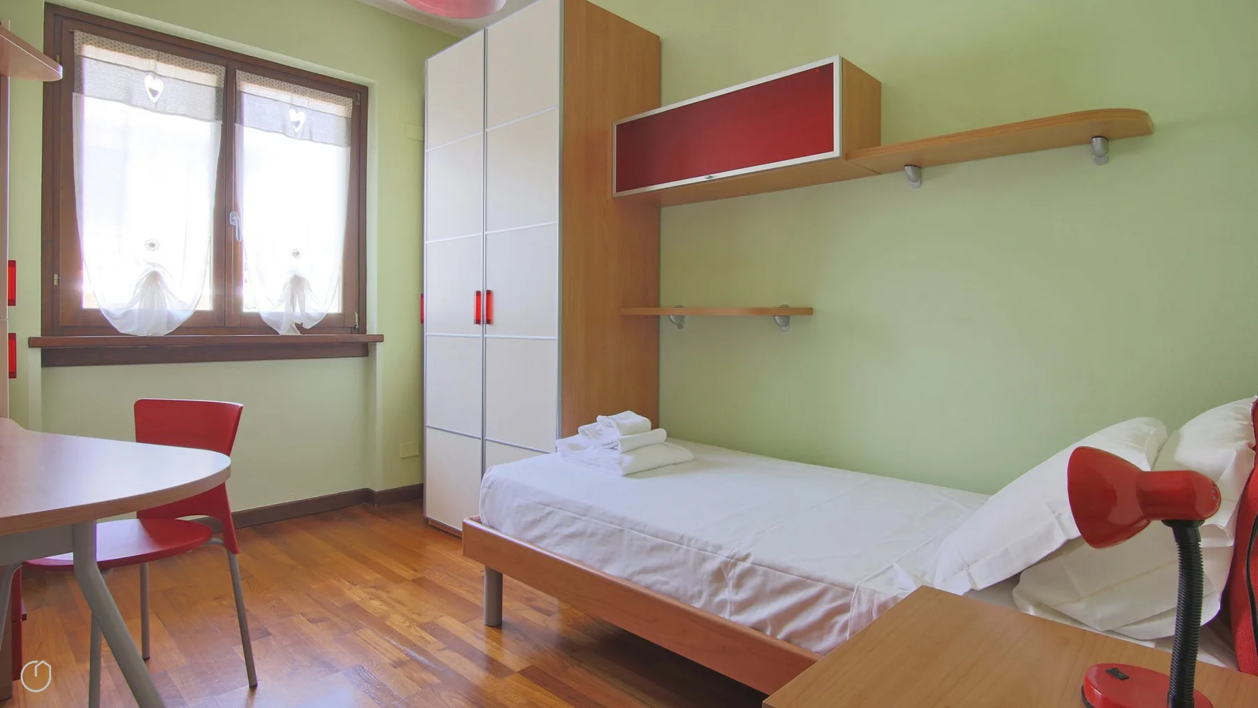 A bedroom with a single bed, a desk, and a window.