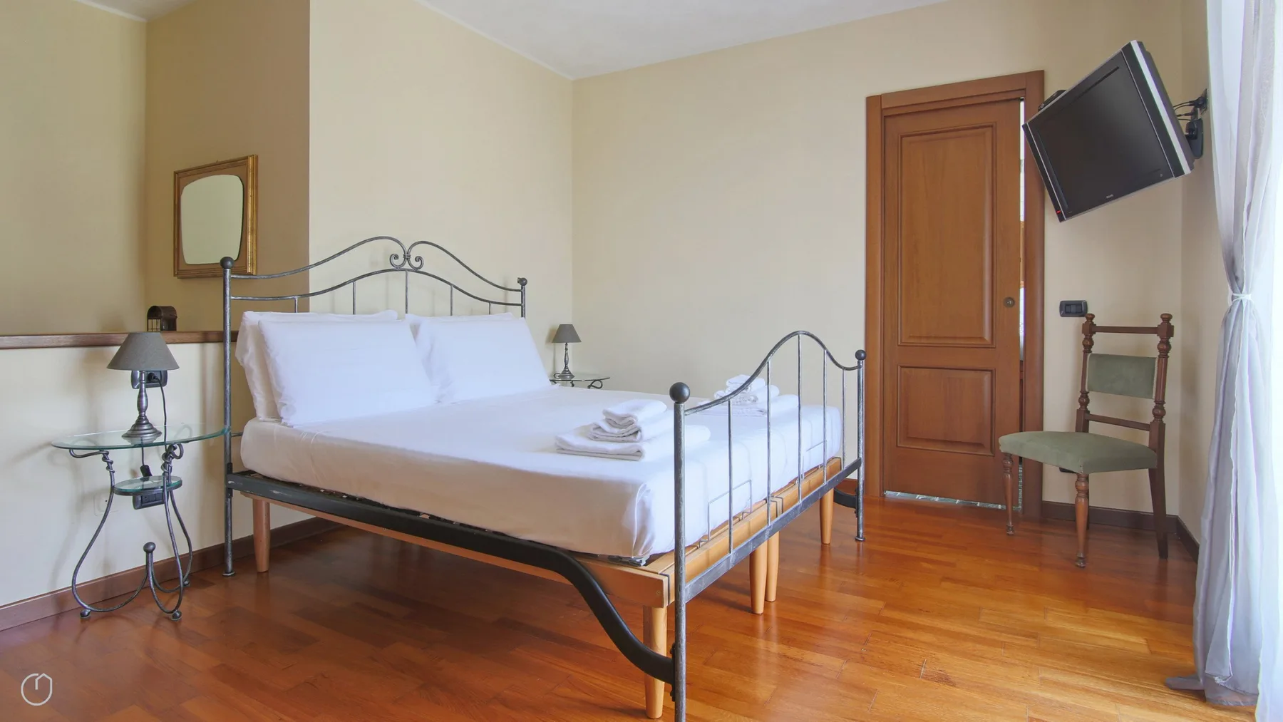 A bedroom with a metal-framed bed, wooden flooring, and a television mounted on the wall.