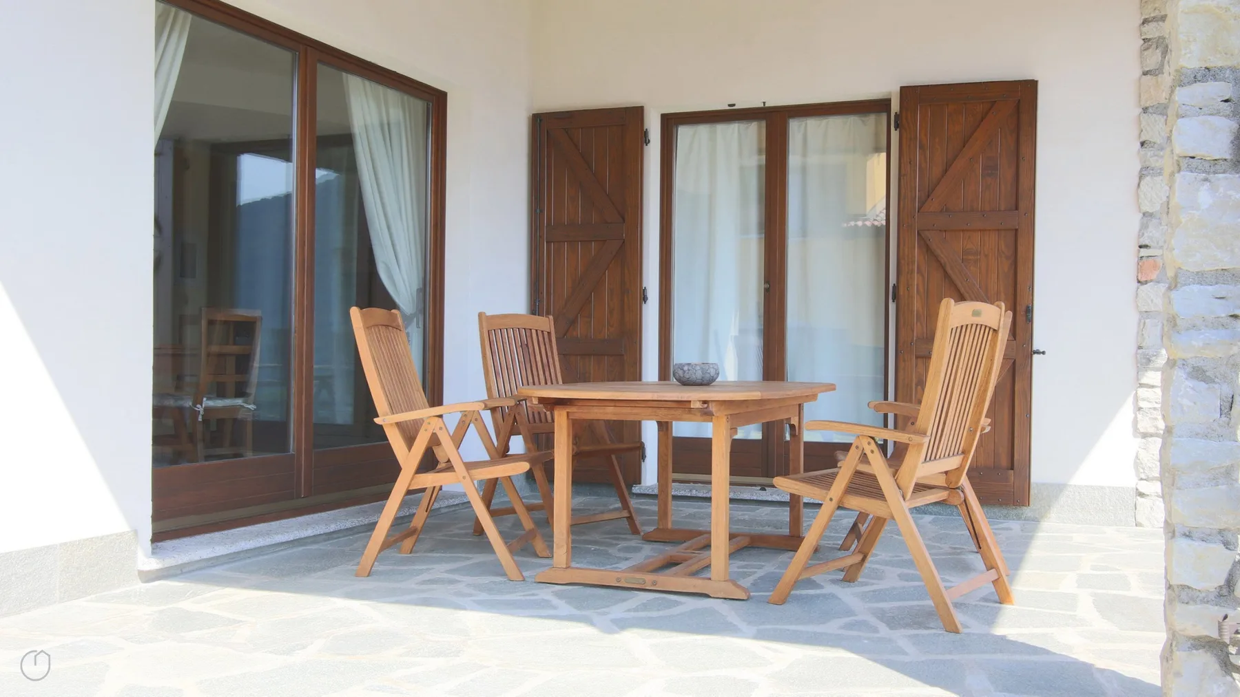 Una zona de estar en el patio con una mesa y sillas de madera junto a puertas de cristal.