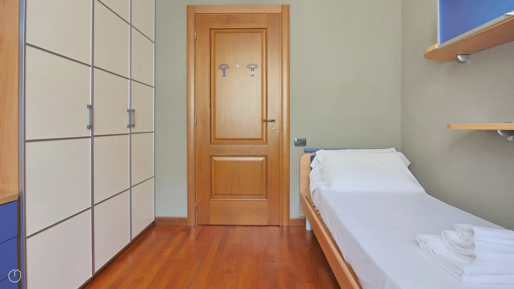 A narrow bedroom with a single bed, wooden door, and built-in wardrobes.