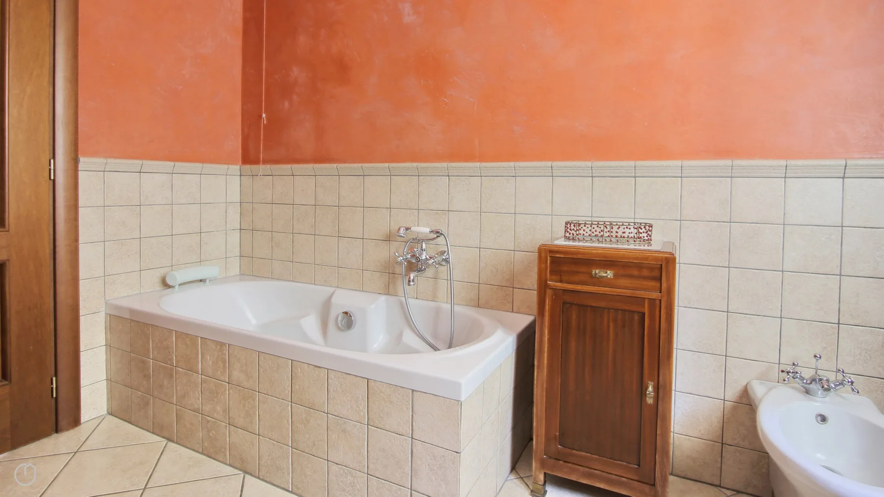 A tiled bathroom with a bathtub, wooden cabinet, and part of a sink.