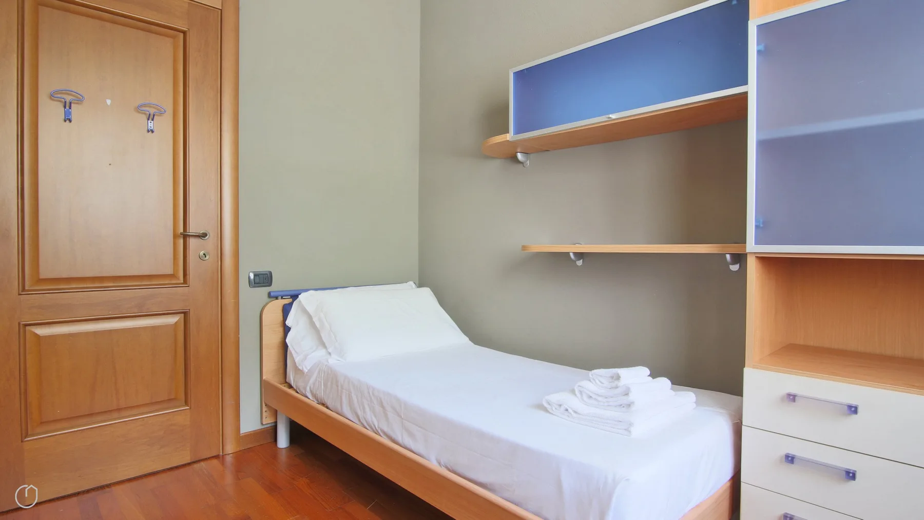 A bedroom with a single bed, a wooden door, and wall-mounted shelves.