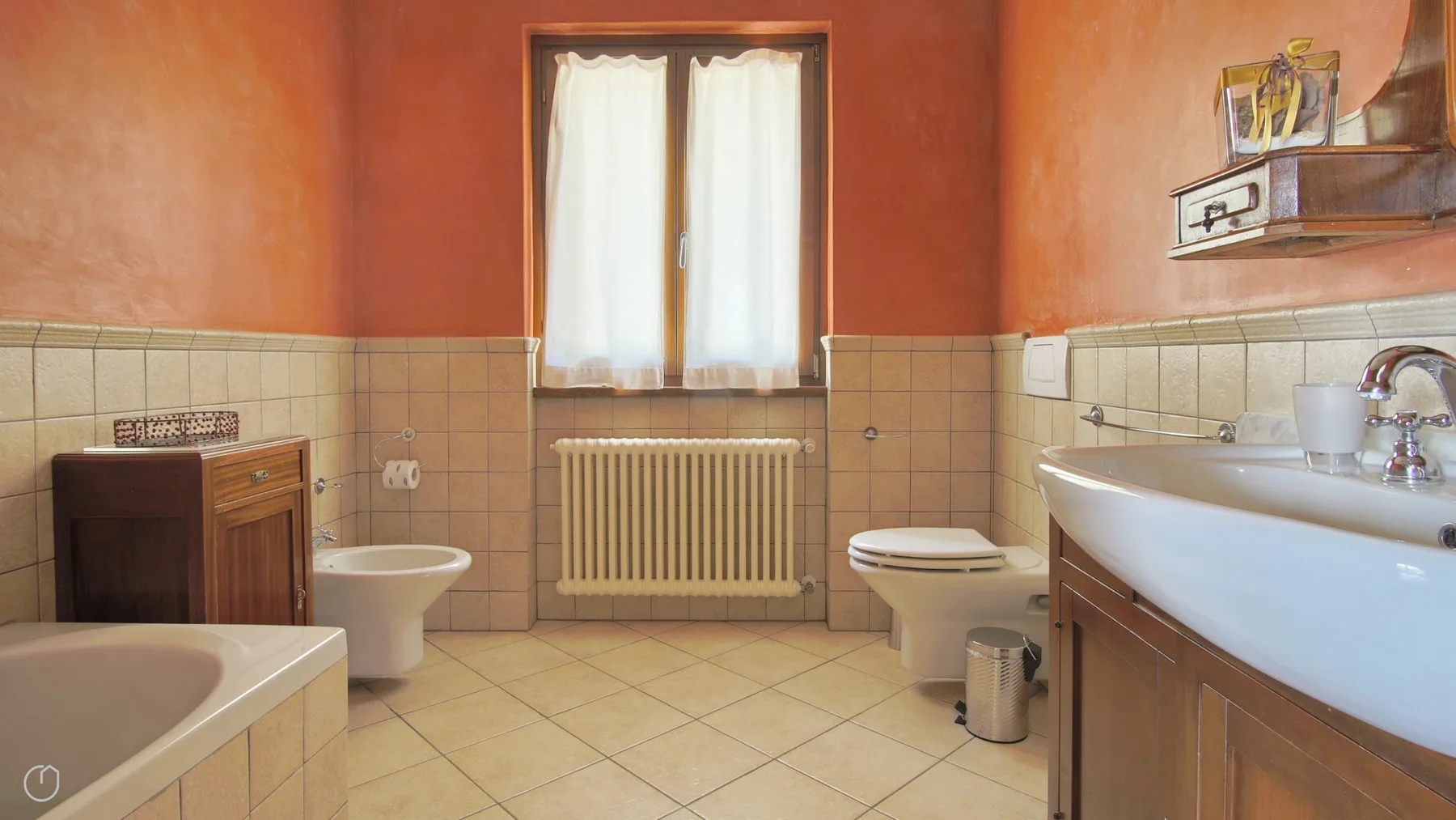 A tiled bathroom with a bathtub, sink, toilet, and curtained window.