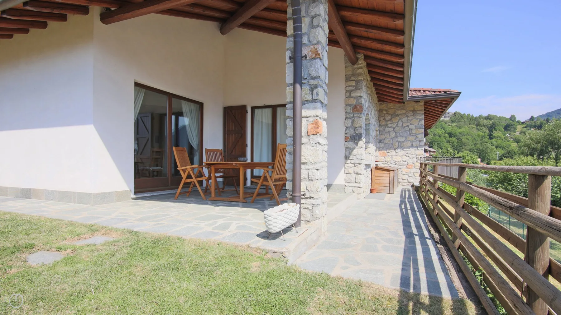 A covered stone patio with wooden seating overlooks a green hillside.