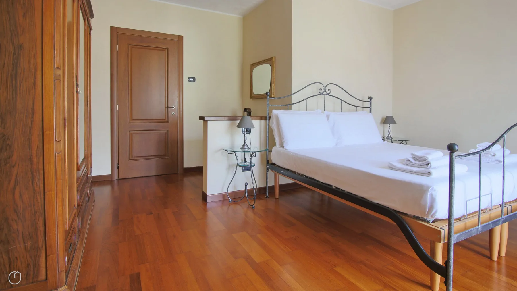 A bedroom with a metal-framed bed, wooden flooring, and a wardrobe.