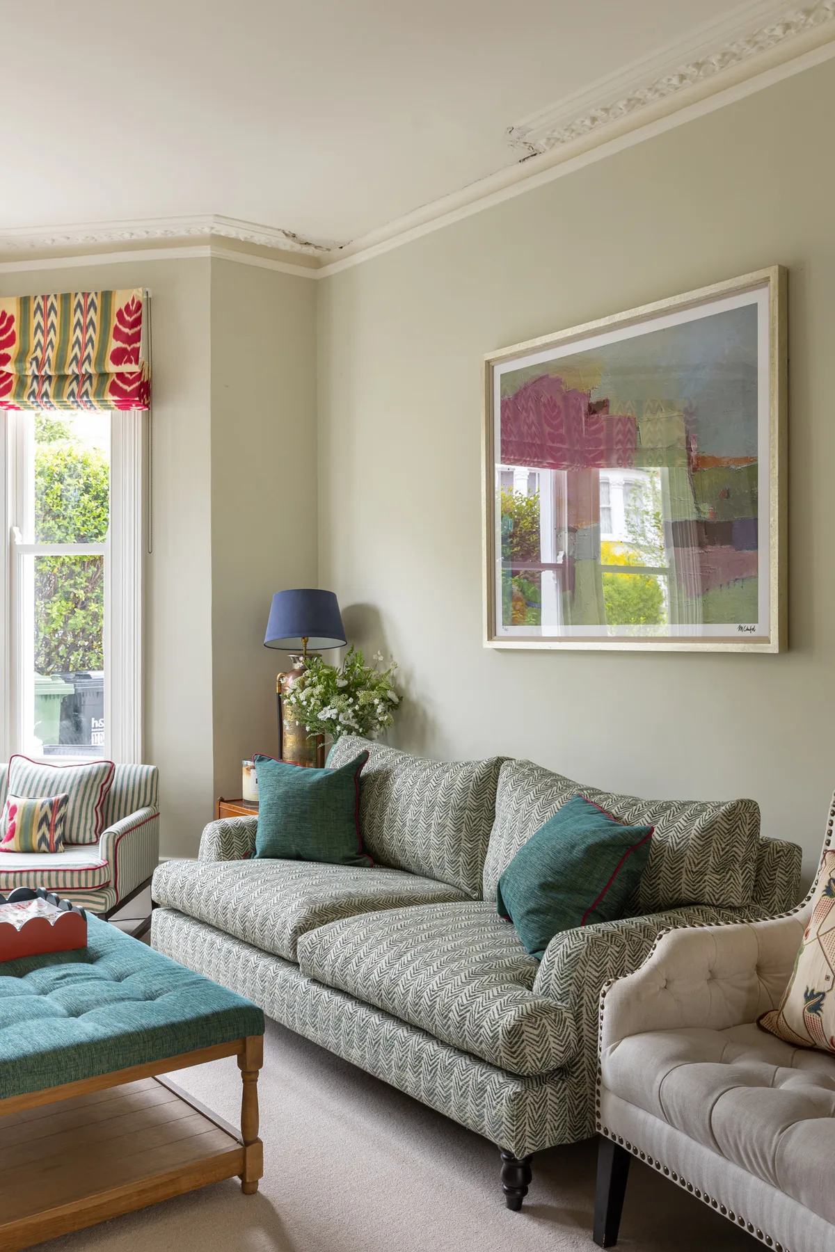 A living room with a patterned sofa, teal cushions, and a framed artwork.