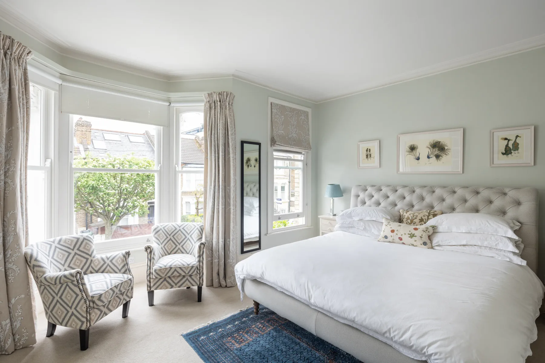 A bright bedroom with a large bed and two patterned seats by the windows.