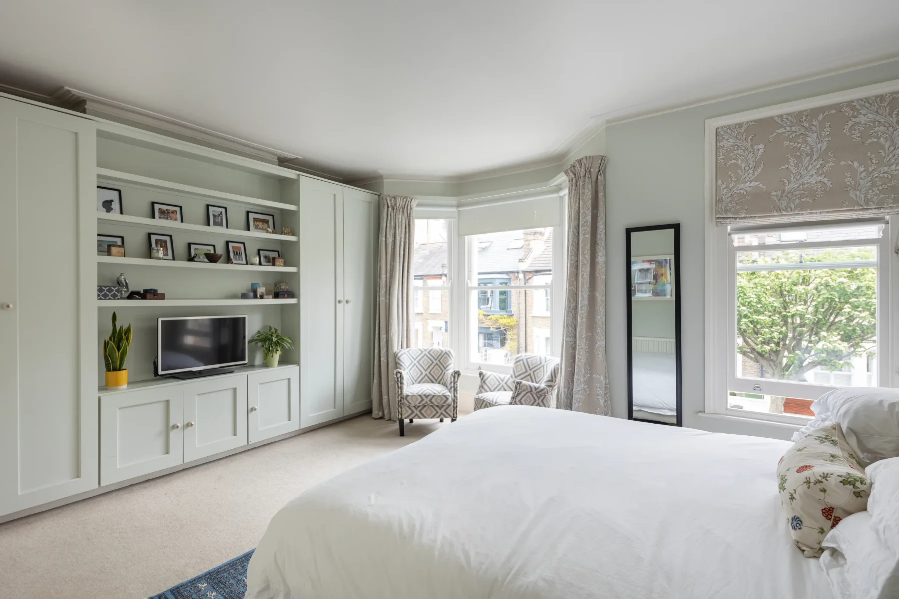 A bright bedroom with a large bed, built-in shelving, and windows.