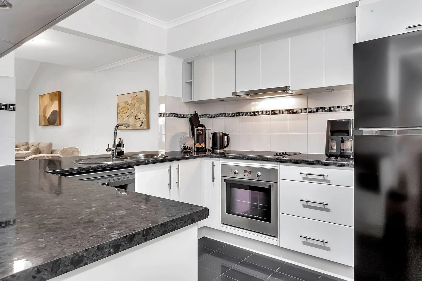 A modern kitchen with white cabinets, dark countertops, and a built-in oven.