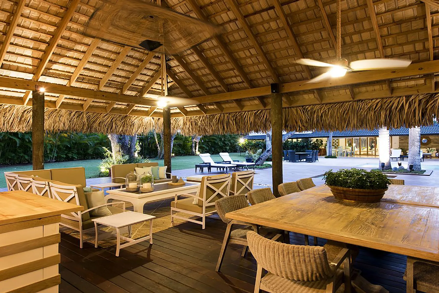 Una zona de comedor al aire libre con mesas de madera bajo un techo de paja.