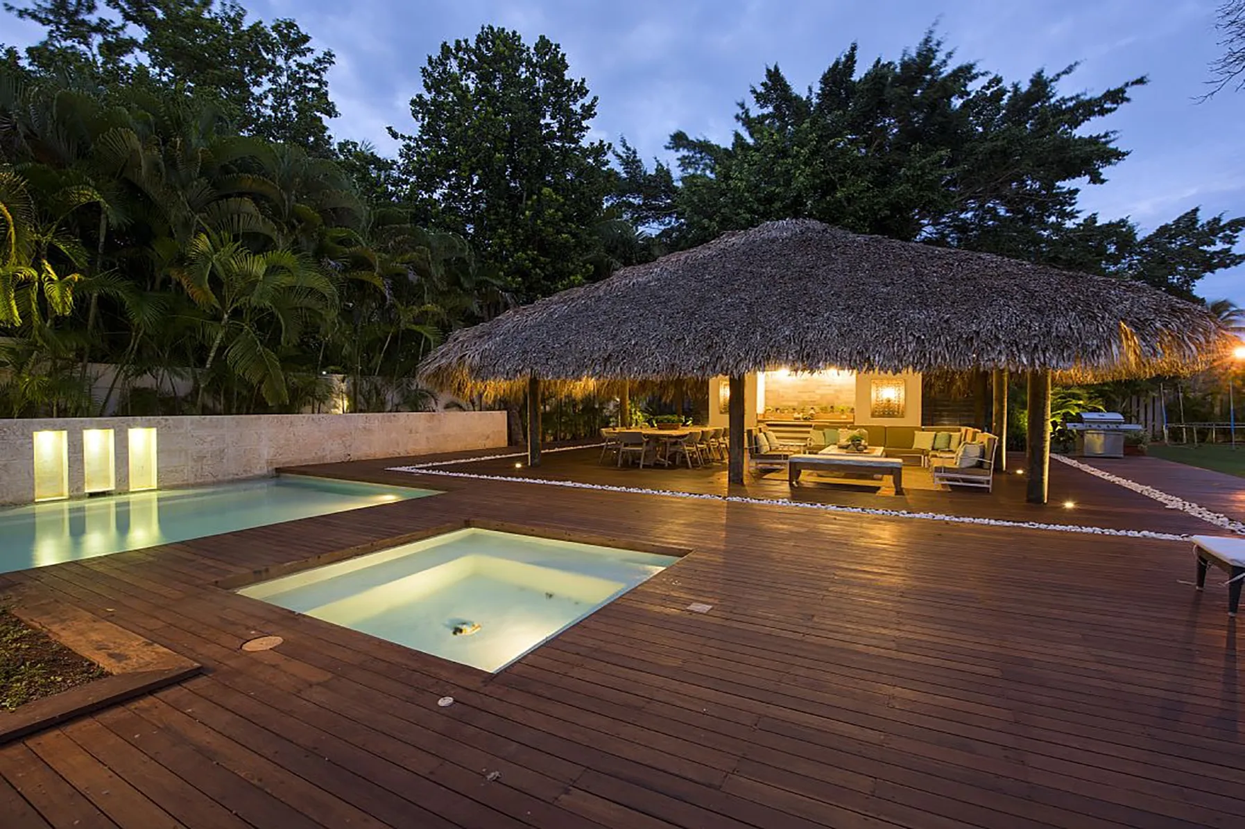 Una piscina al aire libre y una terraza de madera junto a una zona de estar con techo de paja.