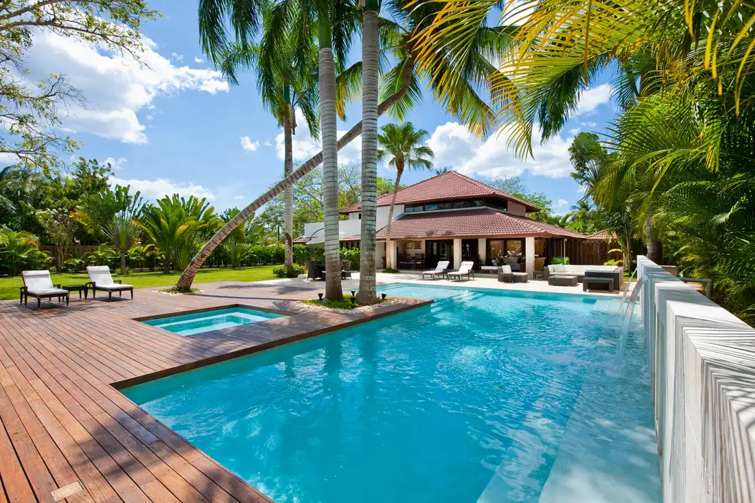 Una piscina tropical al aire libre junto a una terraza de madera y un pabellón sombreado.