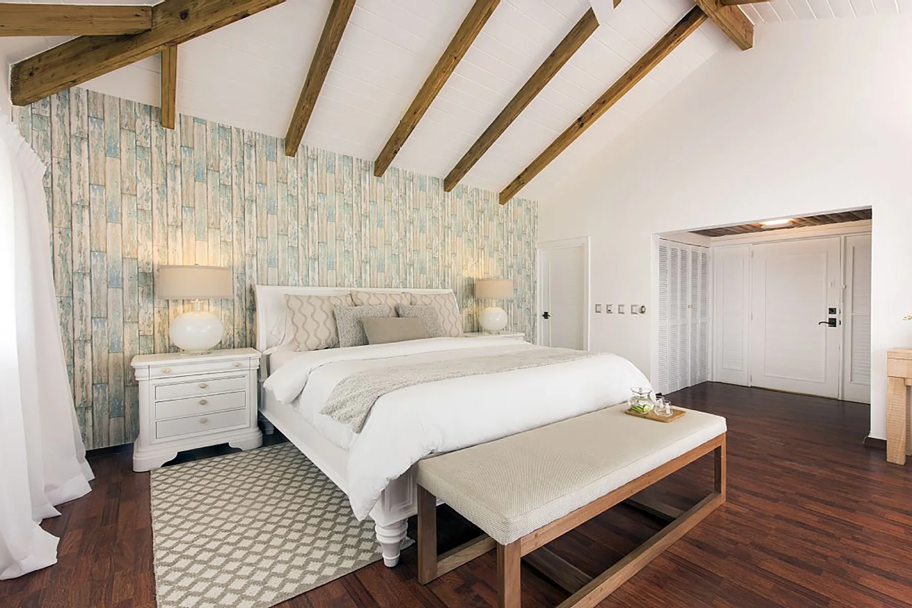 Un dormitorio luminoso con una cama grande y vigas de madera a la vista.