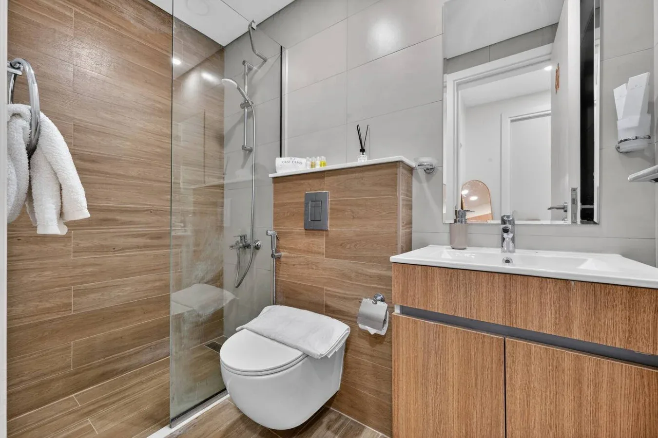 A modern bathroom with a glass shower, toilet, and wood-toned vanity.