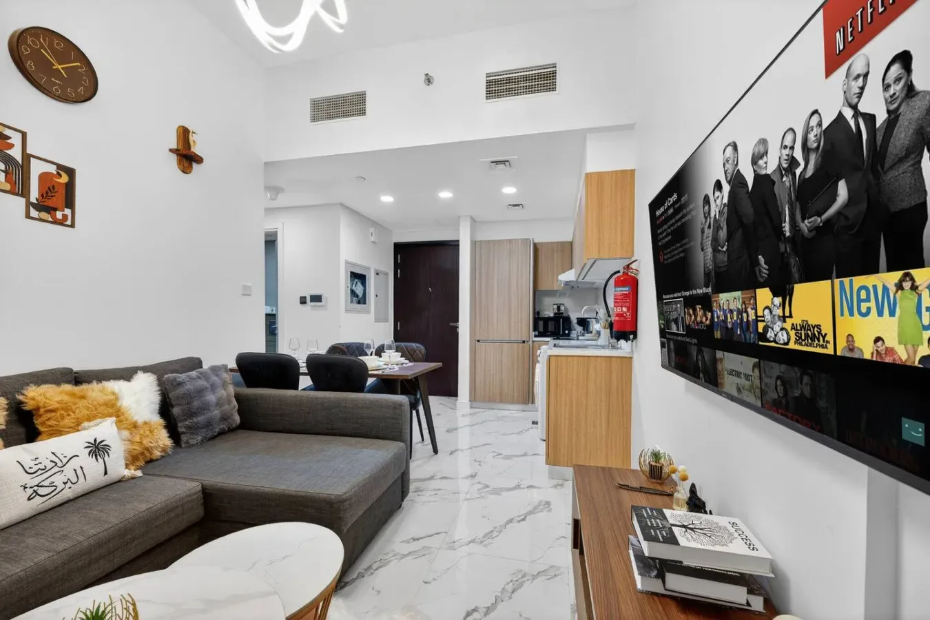 A modern living room with a sectional sofa, dining table, and wall-mounted television.