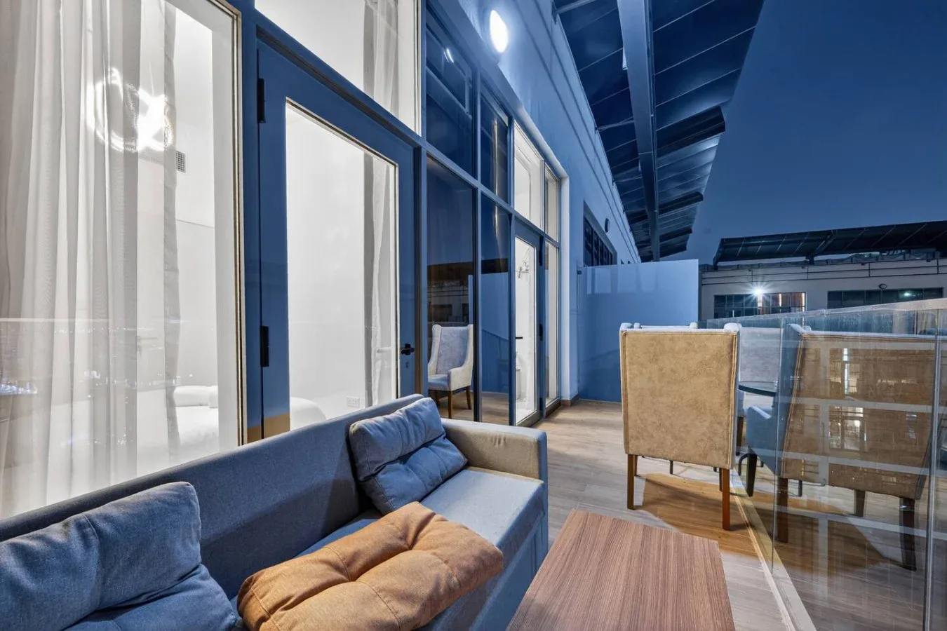 A modern lounge with blue seating beside glass walls and a wooden table.