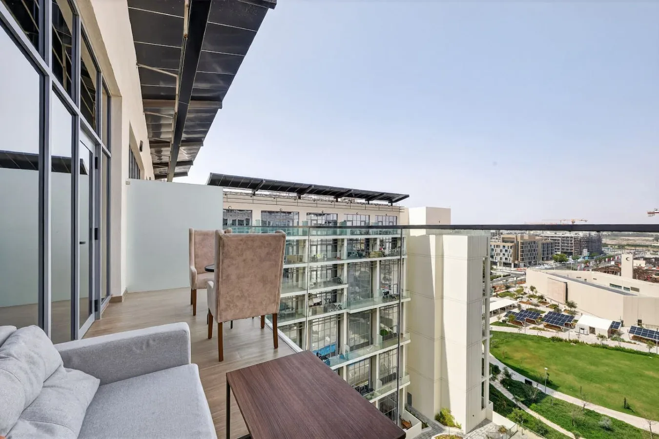 A balcony with seating overlooks a landscaped courtyard and nearby buildings.