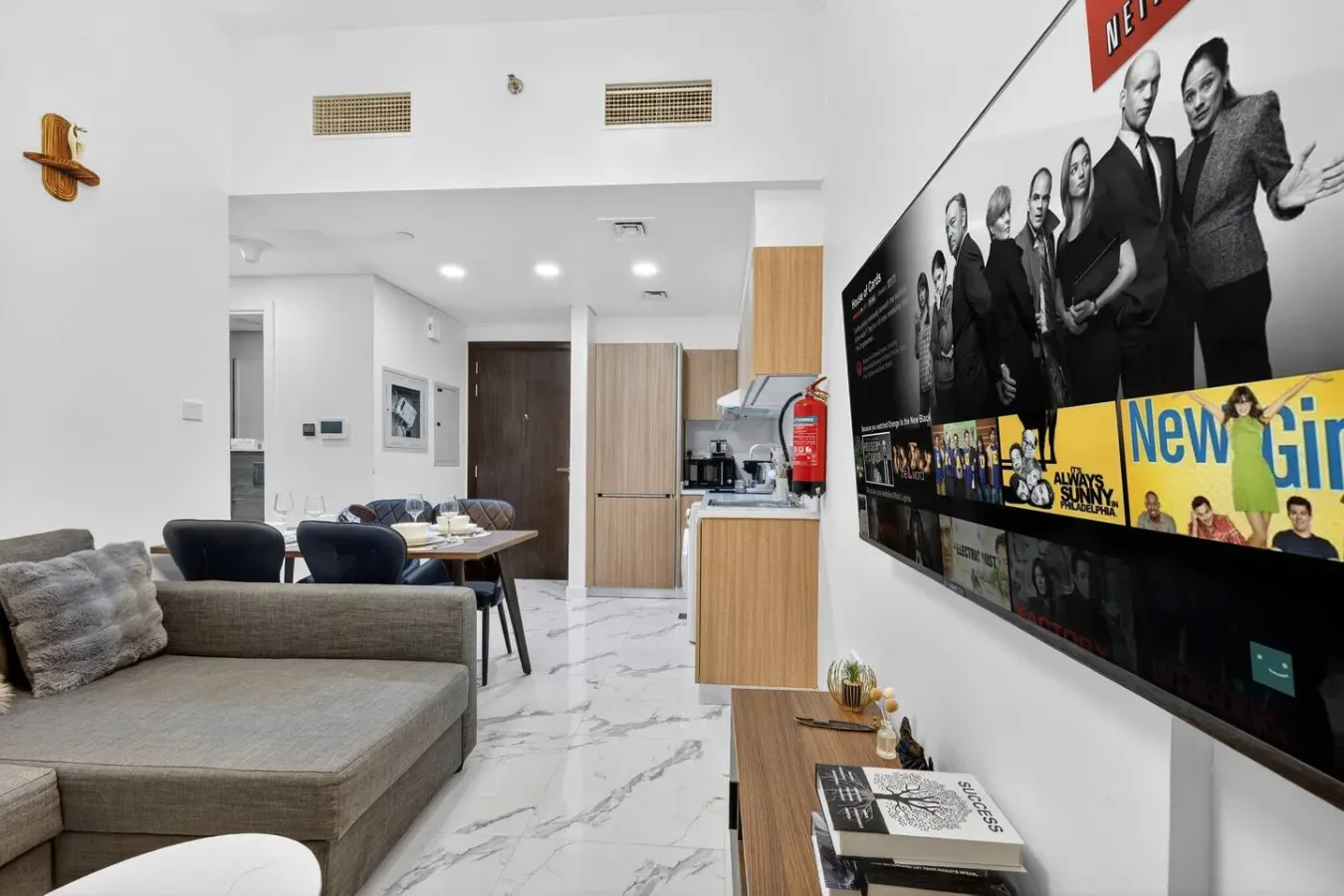 A modern living room with seating, a dining table, and a large wall-mounted television.