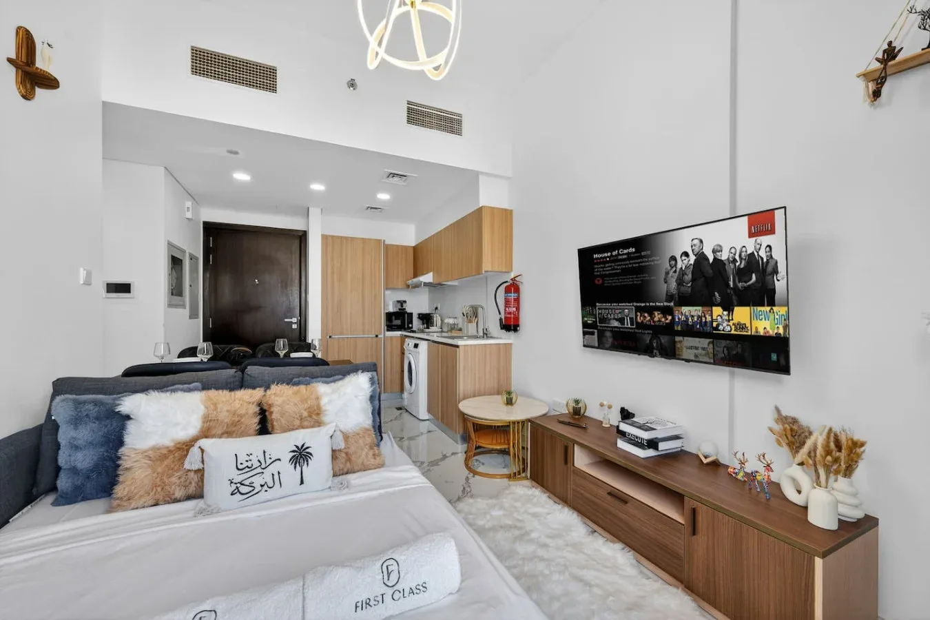 A bright studio room with a bed, kitchenette, and television.