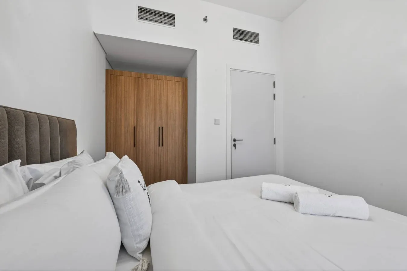 A bright bedroom with a bed, wooden wardrobe, and white door.