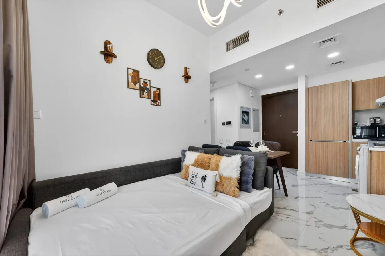 A bedroom with a large bed and a kitchenette visible in the background.