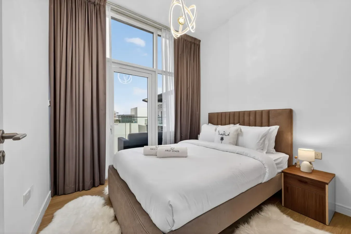 A bright bedroom with a neatly made bed, tall window, and curtains.